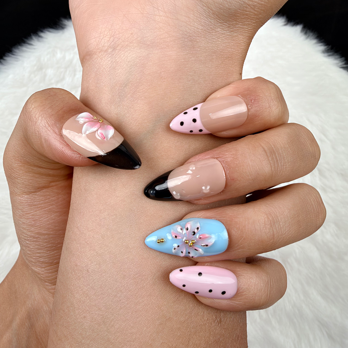 Detail shot of Playful Petals pink, blue and black polka dot floral almond press-on nails on hand