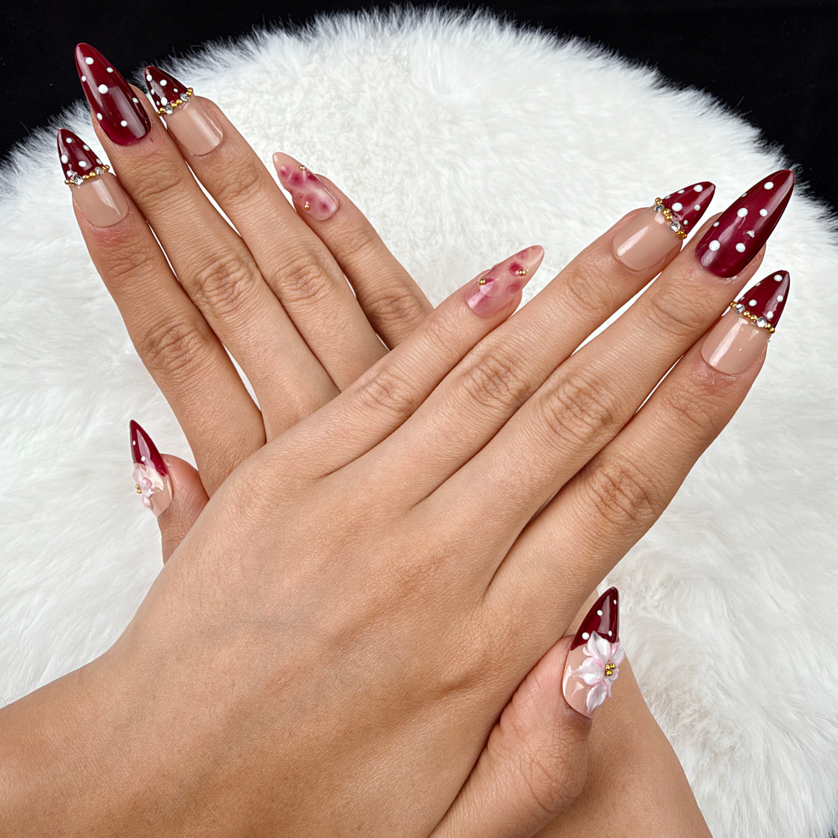 Hands wearing Cherry Blossom burgundy polka dot French tip floral almond press-on nails