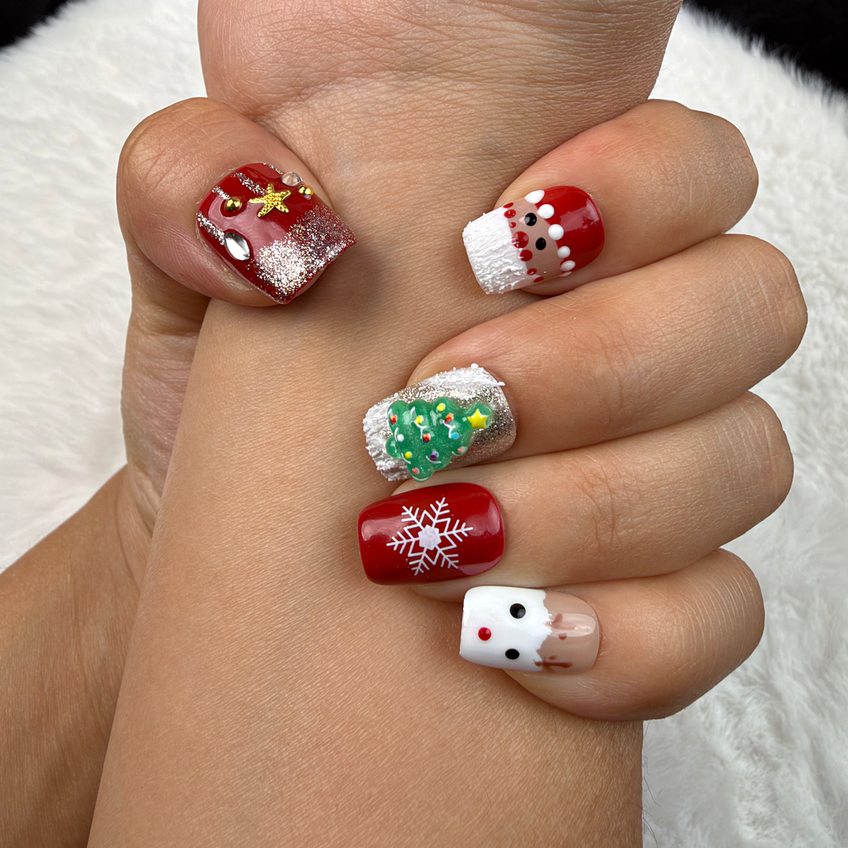 Close-up of hands wearing Christmas Patchwork red and green Christmas square press-on nails with trees and snowflakes
