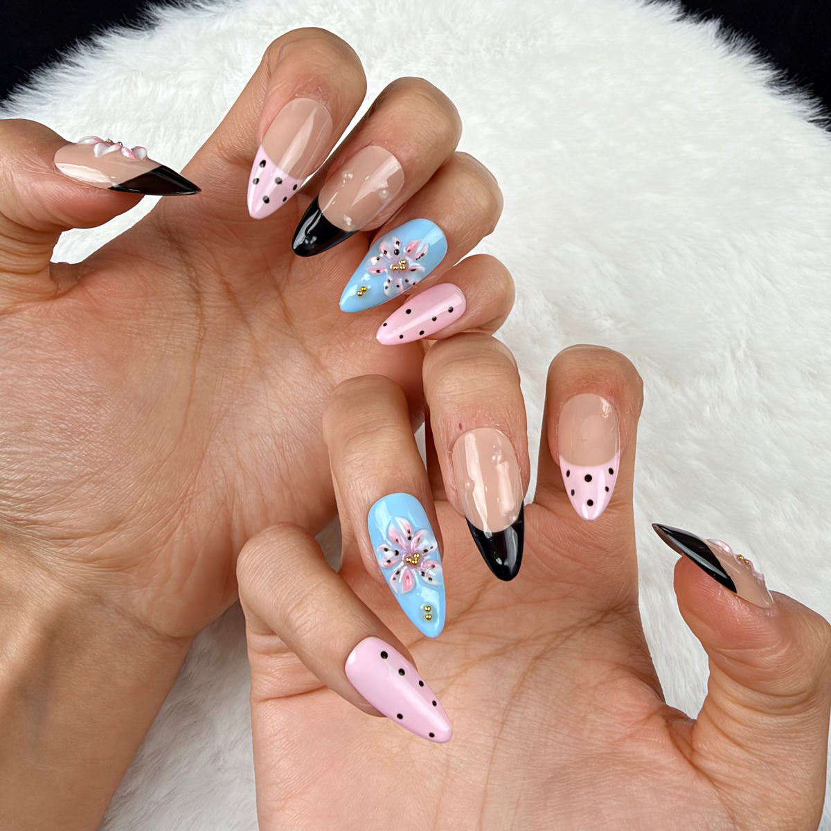 Close-up of hands wearing Playful Petals pink, blue and black polka dot floral almond press-on nails