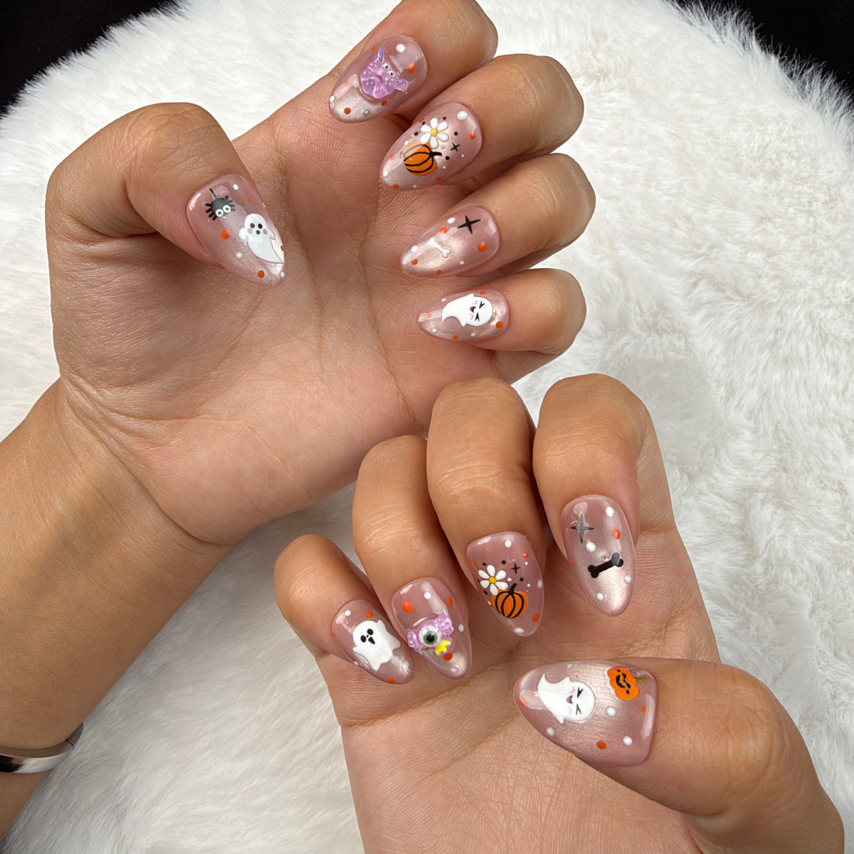 Hands wearing Pastel Haunt nude almond press-on nails with cute ghost and pumpkin Halloween designs