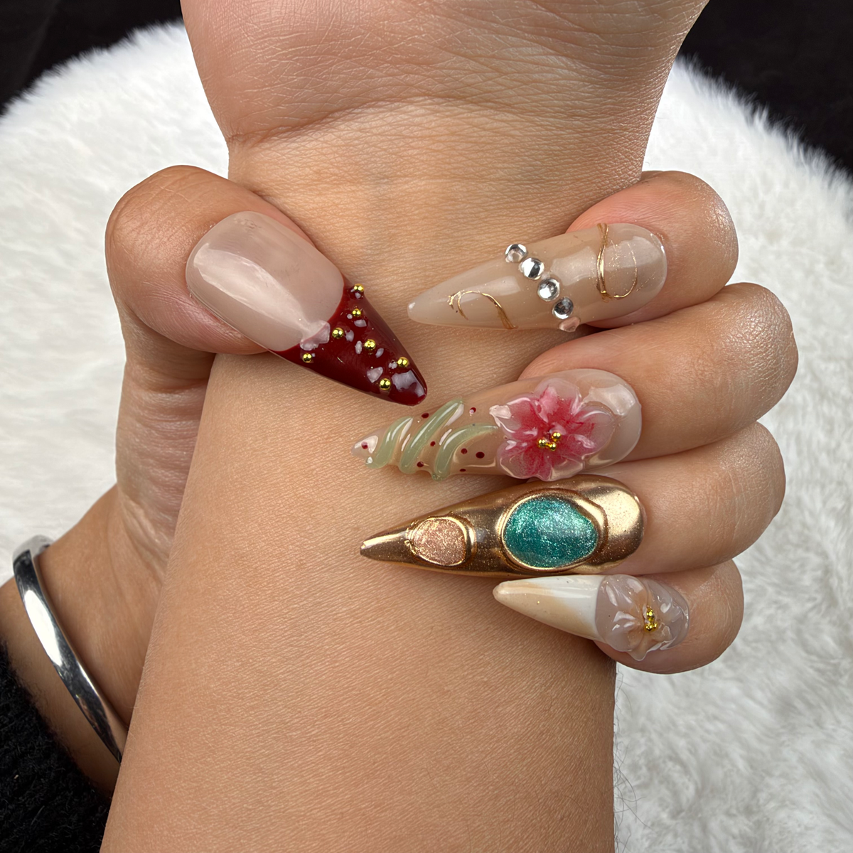 Close-up of hands wearing Gilded Garden nude, burgundy and turquoise floral almond press-on nails with gold accents