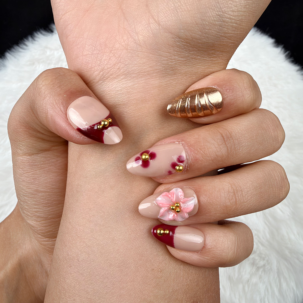 Detail shot of Amber Rose burgundy, gold-tone and pink floral almond press-on nails on hand