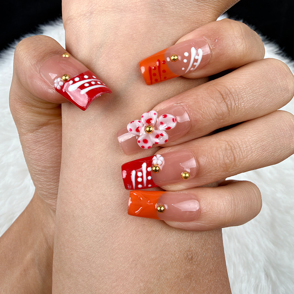 Detail shot of Coral Ribbon coral and orange floral square press-on nails on hand