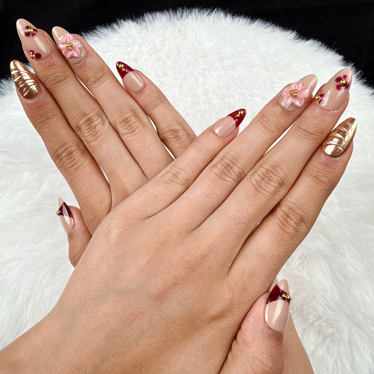 Hands wearing Amber Rose burgundy, gold-tone and pink floral almond press-on nails