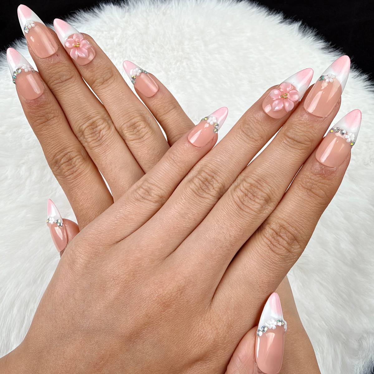 Hands wearing Blush Tiara pink French tip press-on nails with sparkle and floral accents