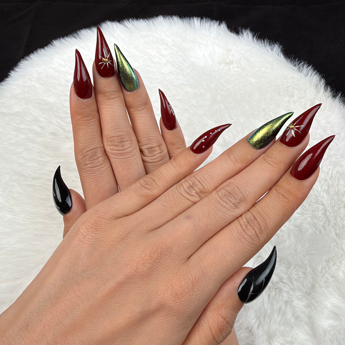 Detail shot of Ruby Orbit burgundy, green chrome and black star stiletto press-on nails on hand