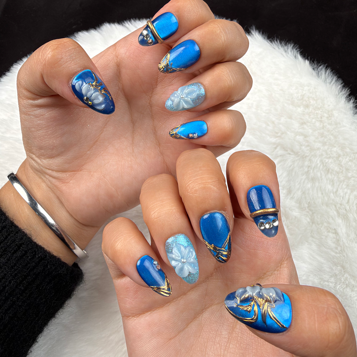 Hands wearing Blue Orchid cobalt and aqua floral almond press-on nails with gold lines