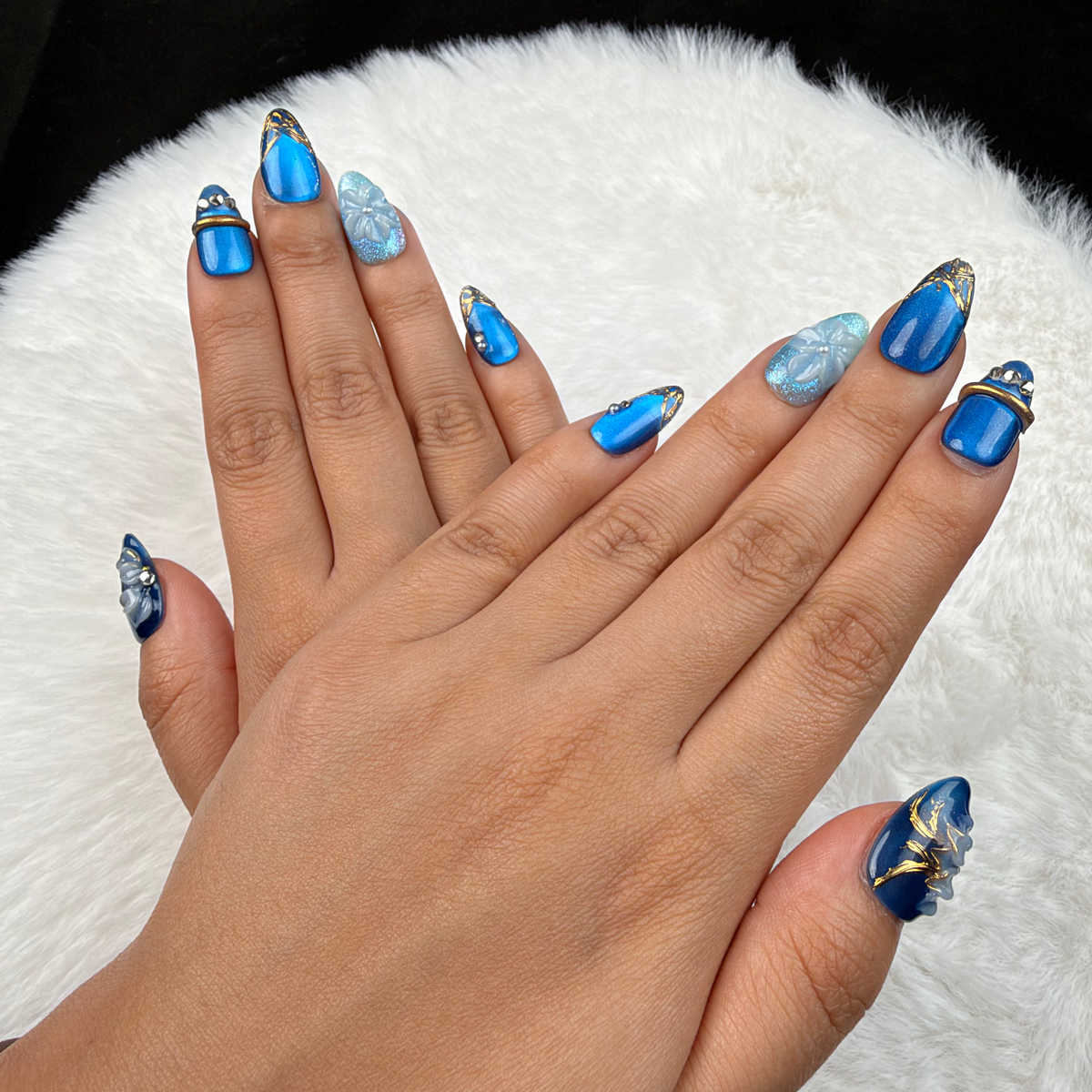Hands wearing Blue Orchid cobalt and aqua floral almond press-on nails with gold lines
