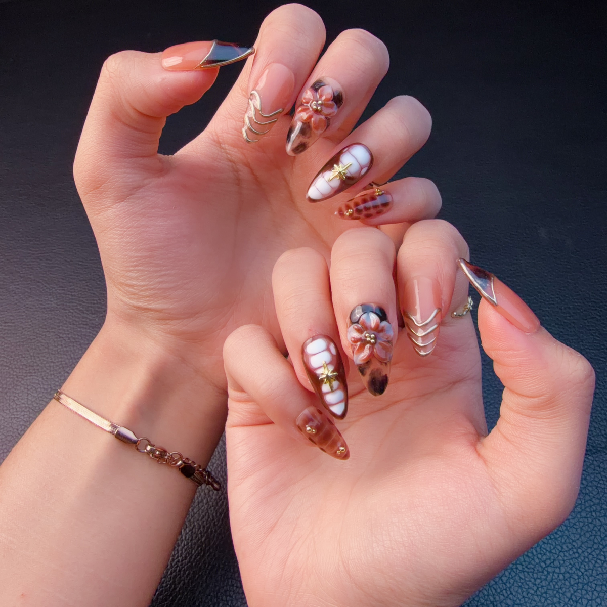 Hands wearing Amber tortoiseshell floral French tip almond press-on nails with gold details