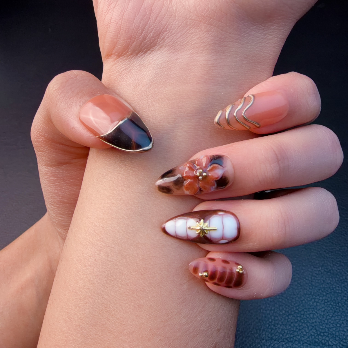 Hands wearing Amber tortoiseshell floral French tip almond press-on nails with gold details