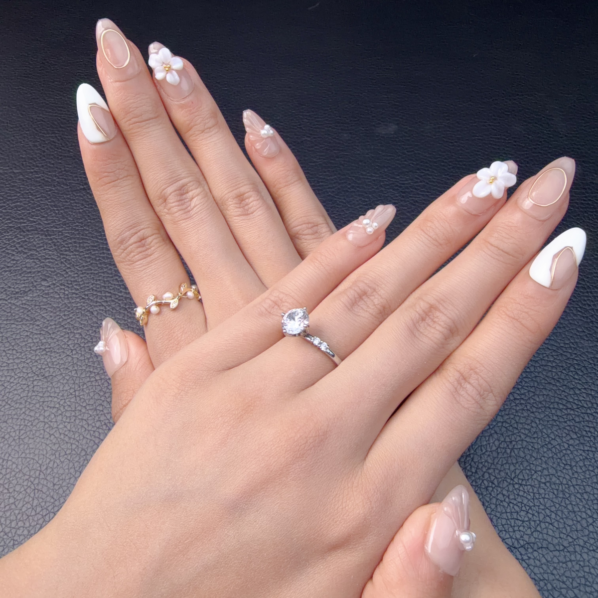 Hands wearing nude pink and white 3D floral medium almond press-on nails with pearls and gold line accents