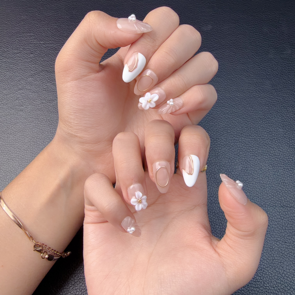 Hands wearing nude pink and white 3D floral medium almond press-on nails with pearls and gold line accents