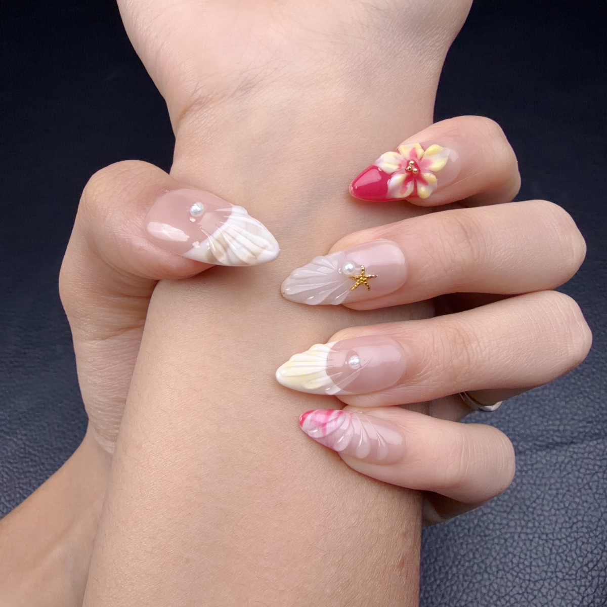 Hands wearing Pink 3D floral seashell medium almond press-on nails with pearls and gold starfish