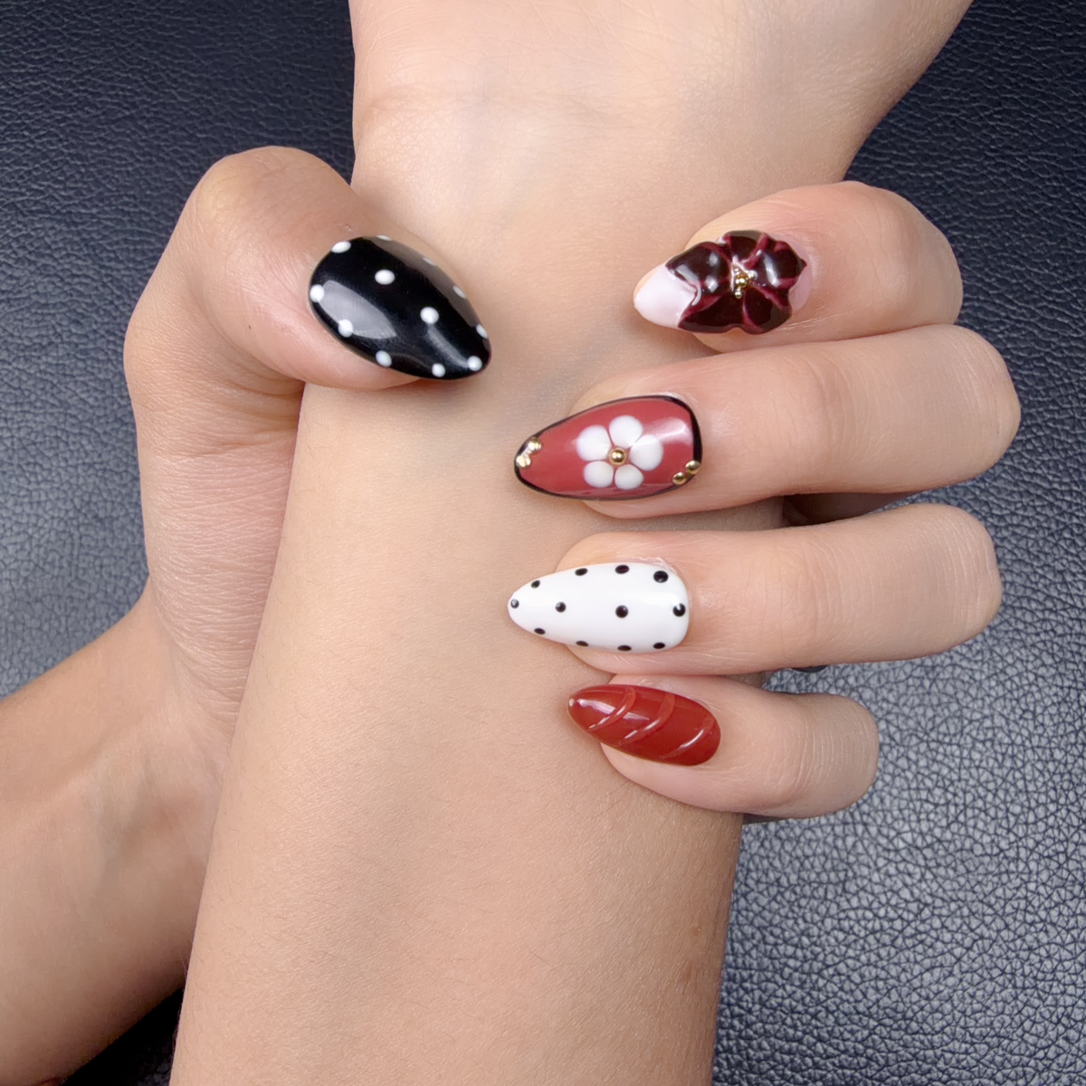 Hands wearing Burgundy and black 3D floral medium almond press-on nails with white flowers