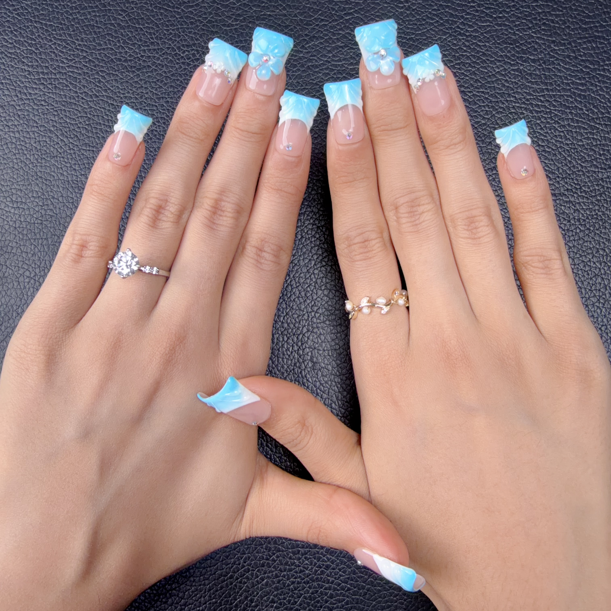 Hands wearing baby blue French tip square press-on nails with a 3D flower and rhinestones