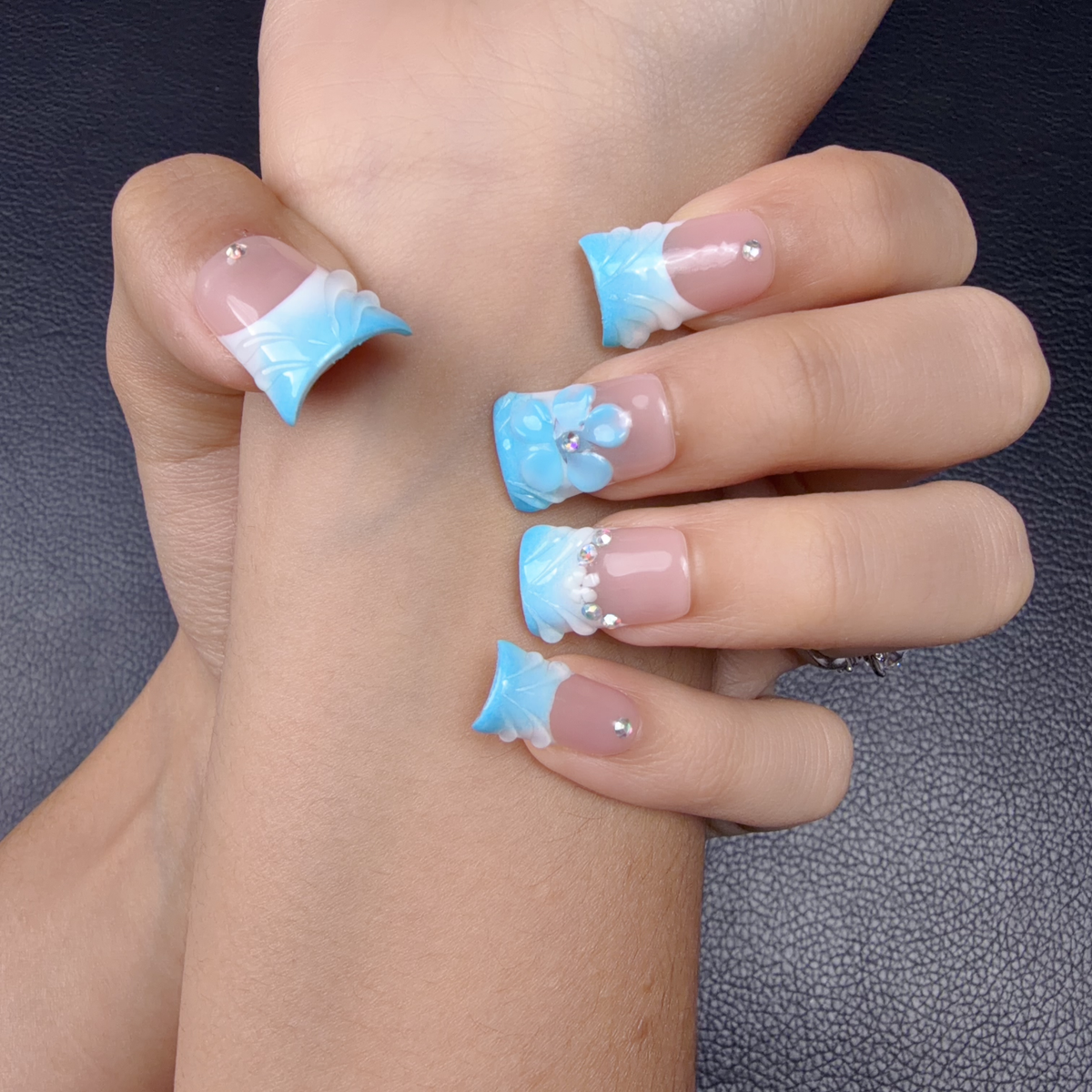 Hands wearing baby blue French tip square press-on nails with a 3D flower and rhinestones