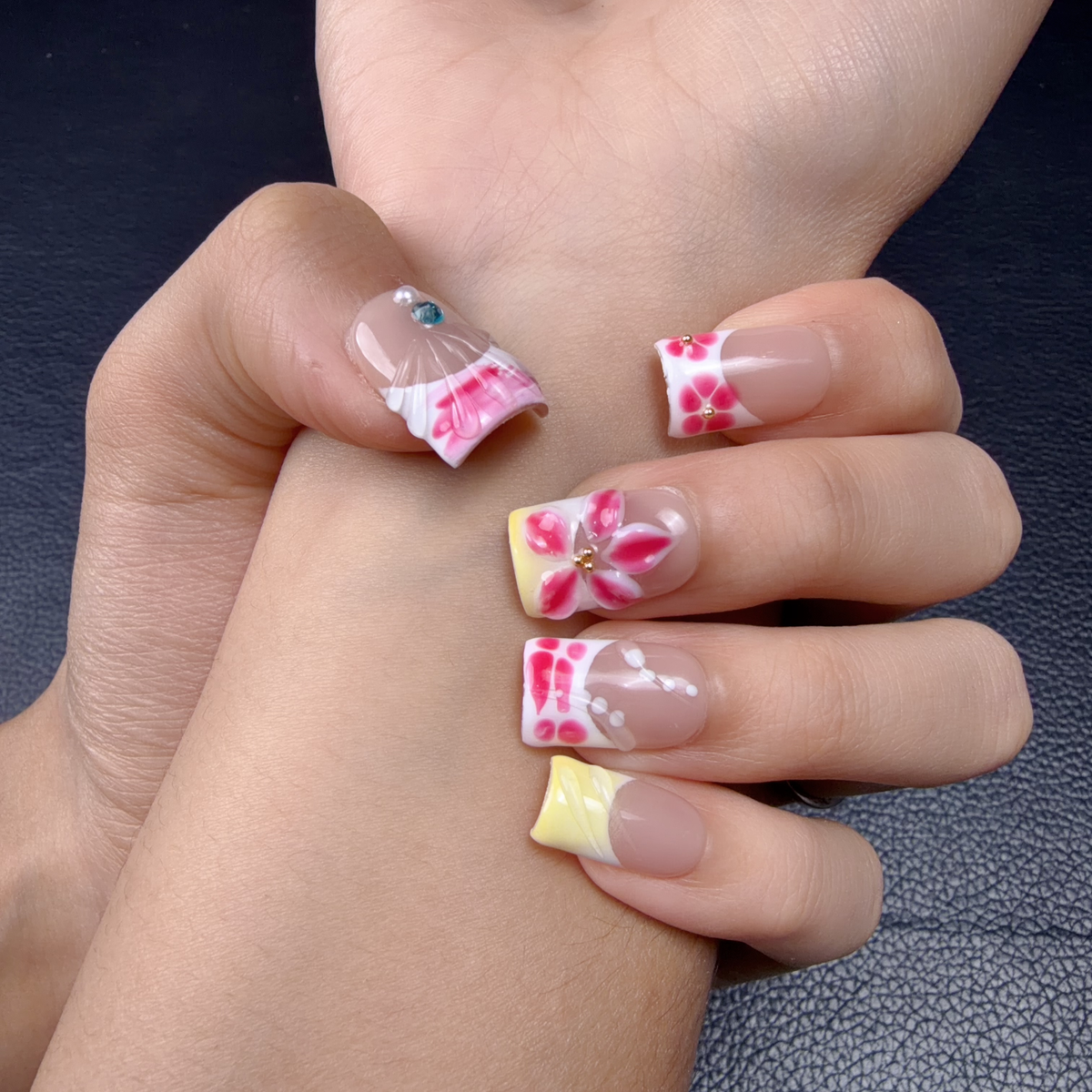 Hands wearing Pink heart graphic floral almond press-on nails with yellow French accents