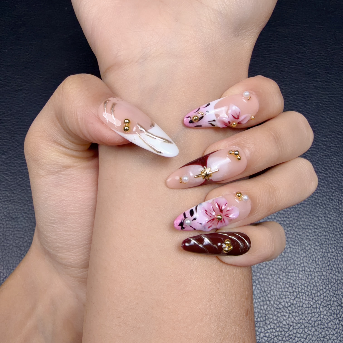 Hands wearing Blush and wine red floral bow almond press-on nails with gold details
