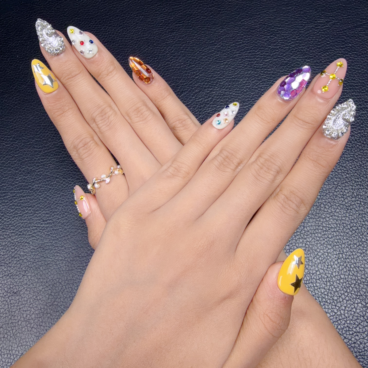 Hands wearing Cosmic Candy Y2K jeweled medium almond press-on nails with celestial details