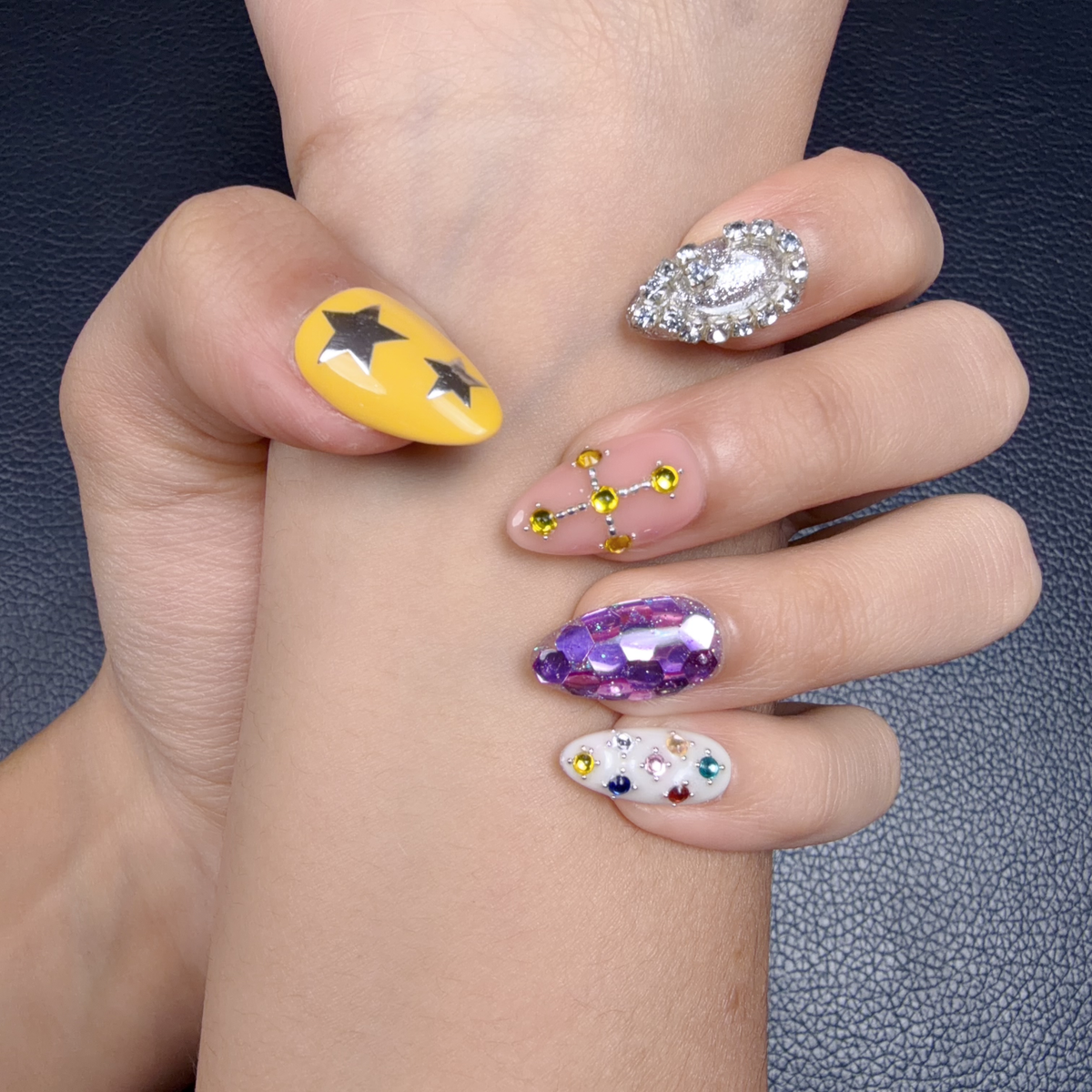 Hands wearing Cosmic Candy Y2K jeweled medium almond press-on nails with celestial details