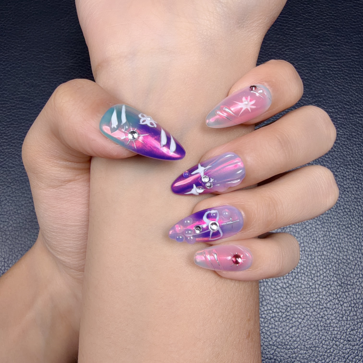 Hands wearing Aurora Ribbon pink, violet and icy blue celestial chrome press-on nails