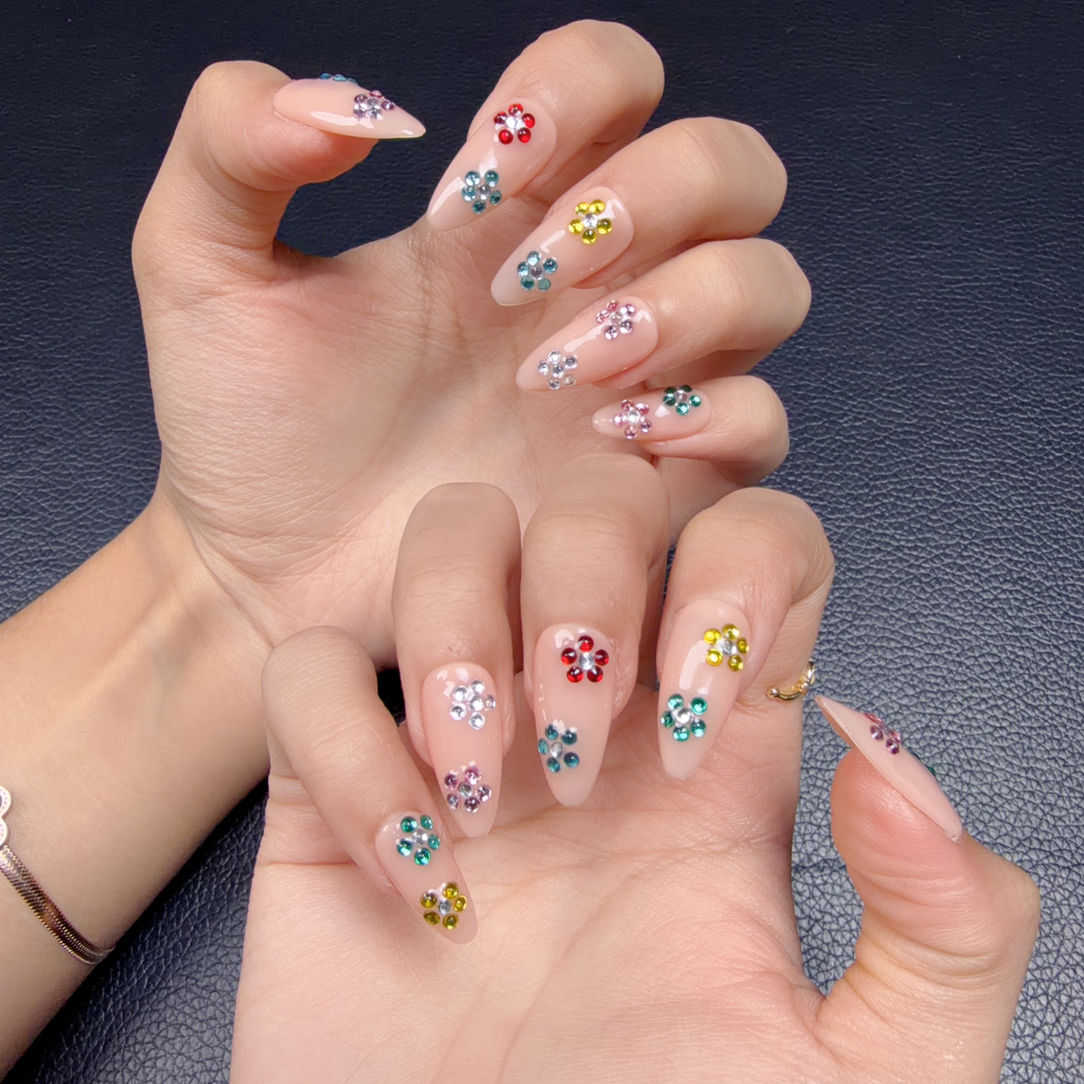 Hands wearing Sticker Party nude pink medium almond press-on nails with colorful rhinestone flowers