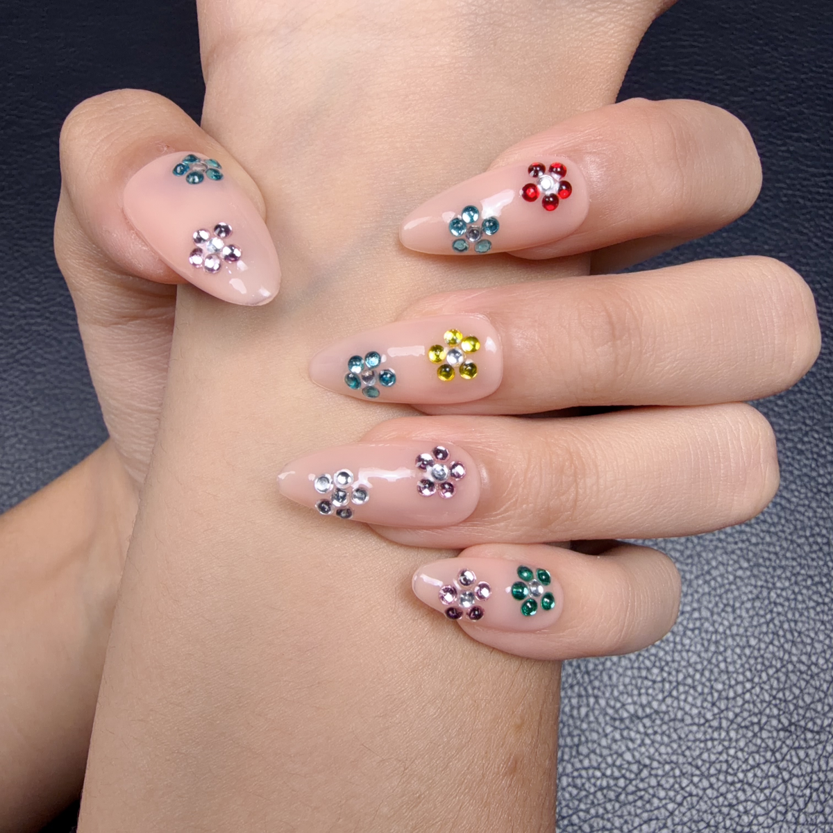 Hands wearing Sticker Party nude pink medium almond press-on nails with colorful rhinestone flowers