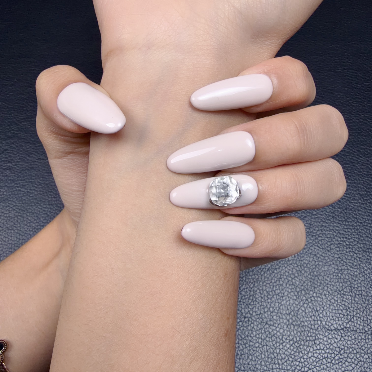 Hands wearing Bare Jewel milky beige press-on nails with a large crystal accent