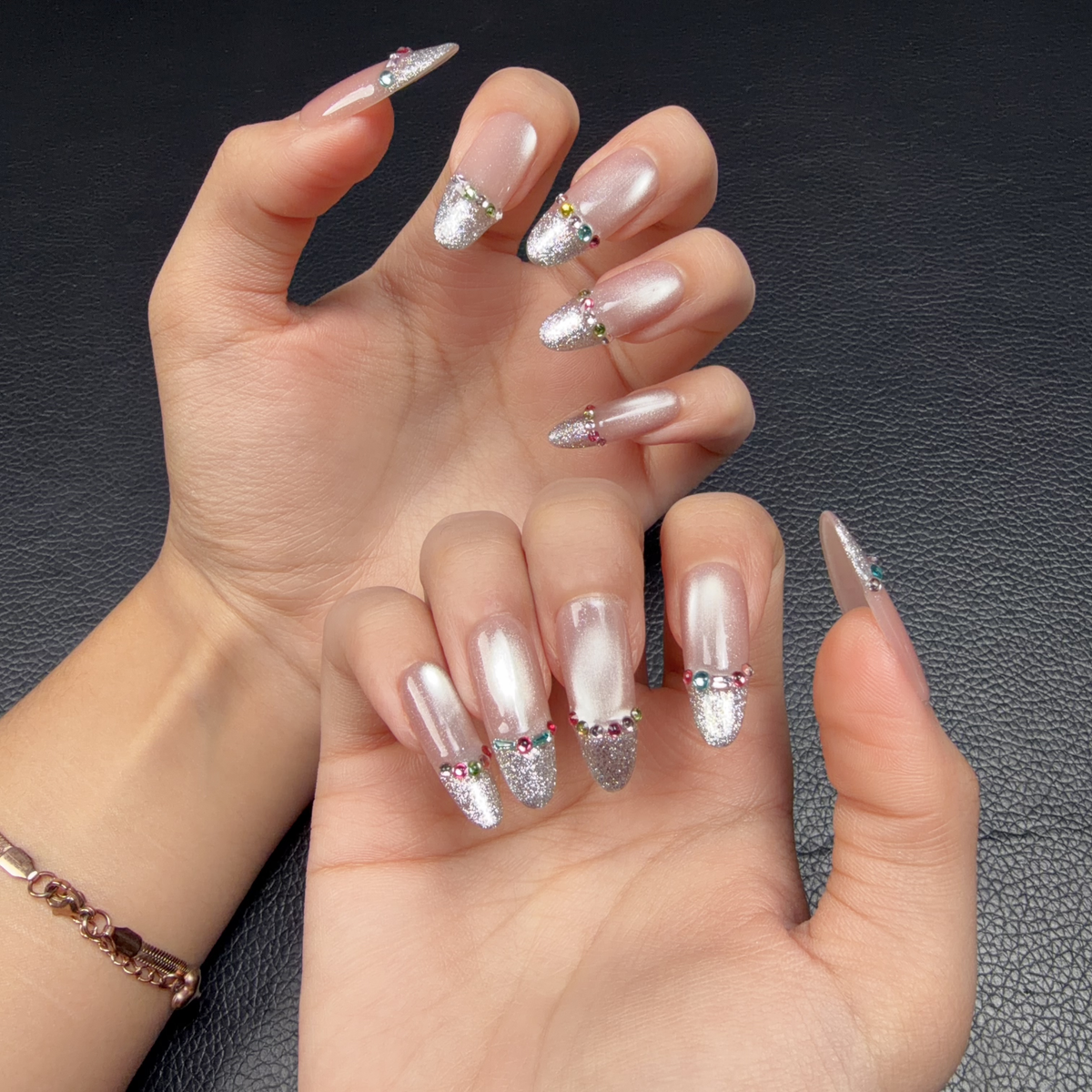 Hands wearing Silver Veil nude pink and silver French tip medium oval press-on nails with rhinestones