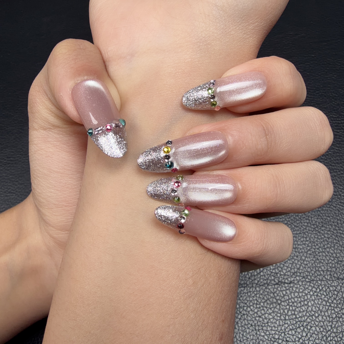 Hands wearing Silver Veil nude pink and silver French tip medium oval press-on nails with rhinestones