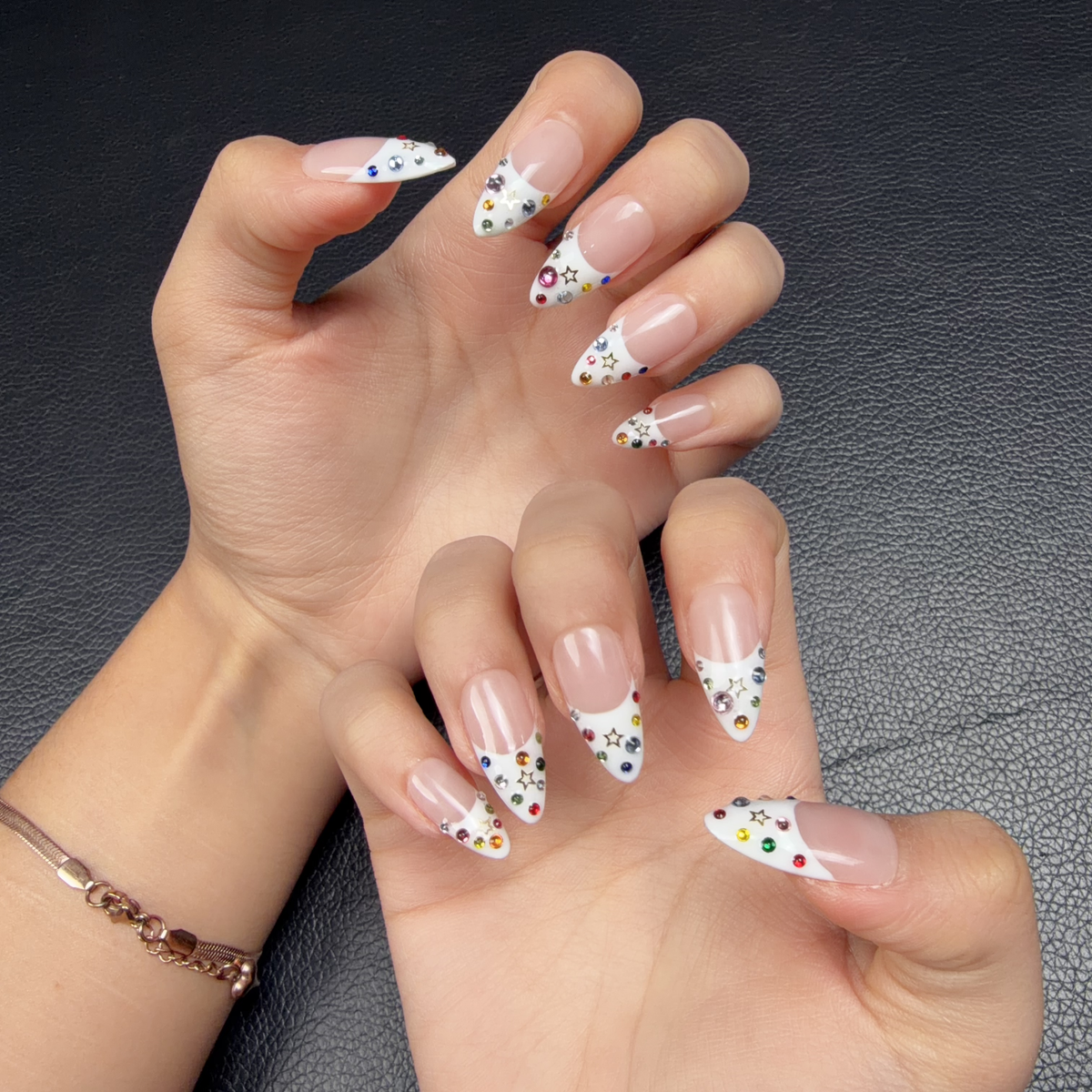 Hands wearing White French tip almond press-on nails with colorful rhinestones and star accents