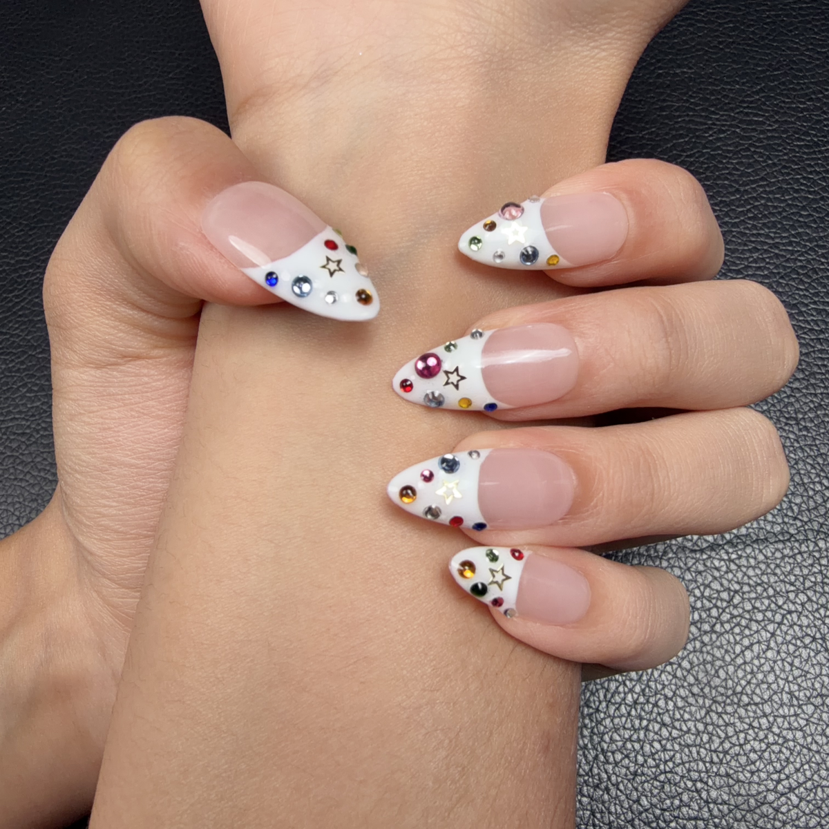 Hands wearing White French tip almond press-on nails with colorful rhinestones and star accents