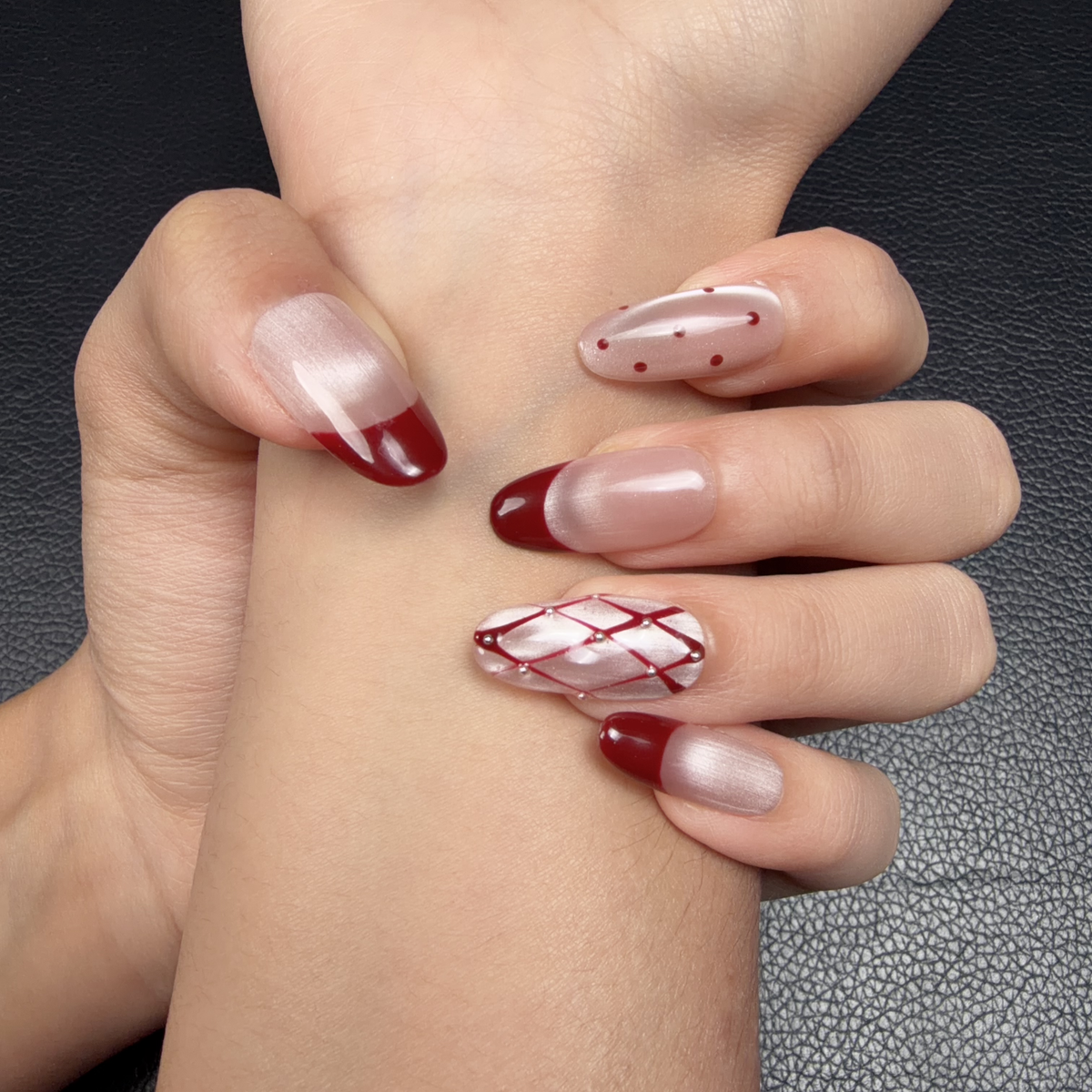 Hands wearing Merlot Lattice burgundy French tip medium oval press-on nails with a crystal accent