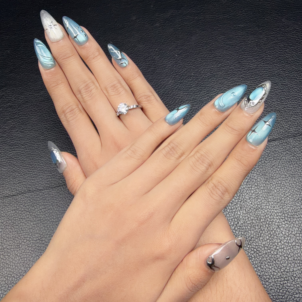 Hands wearing Blue Orbit icy blue cat eye celestial almond press-on nails with silver details