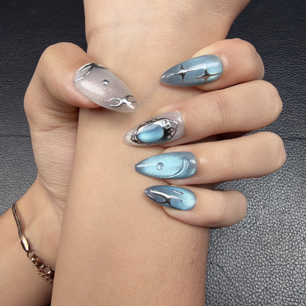 Hands wearing Blue Orbit icy blue cat eye celestial almond press-on nails with silver details