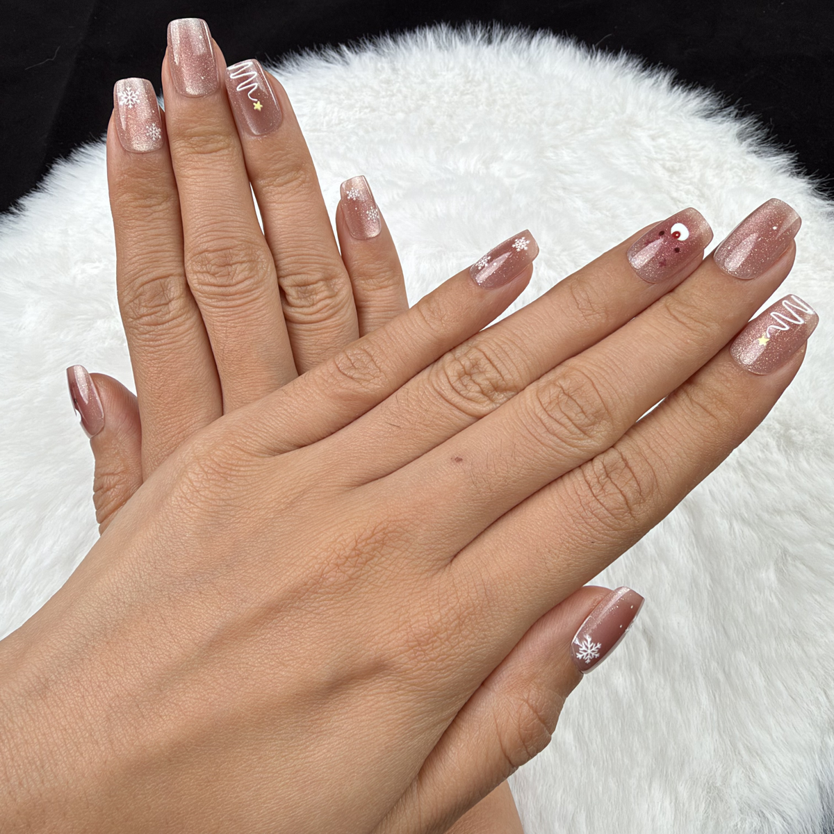 Close-up of hands wearing Reindeer Glow rose nude Christmas square press-on nails with silver reindeer and stars