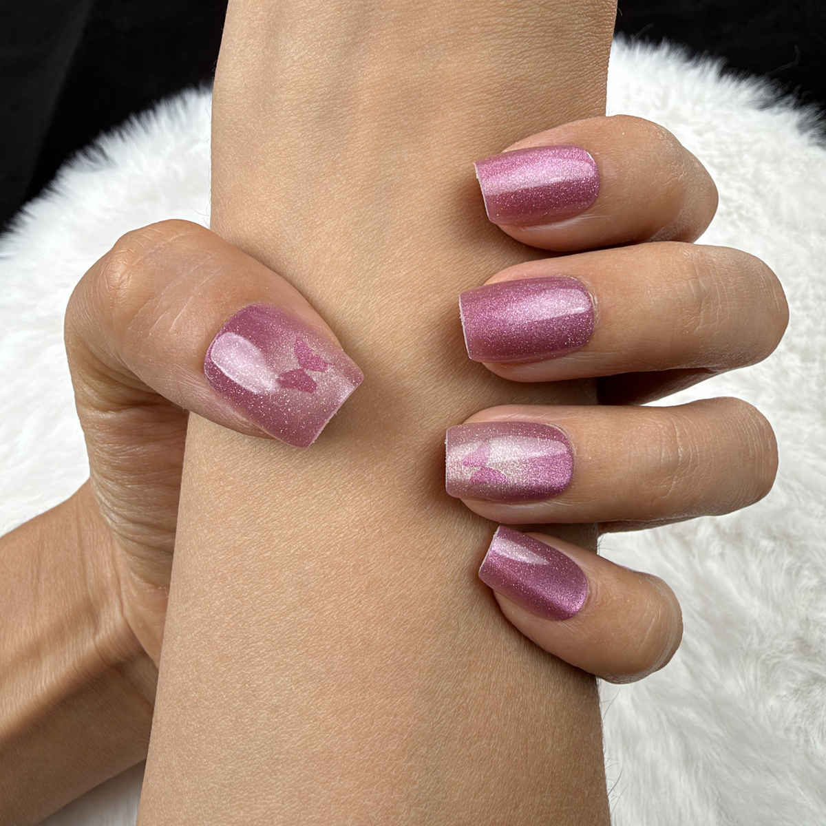 Close-up of hands wearing Rose Wings rose pink cat eye square press-on nails with butterfly accents