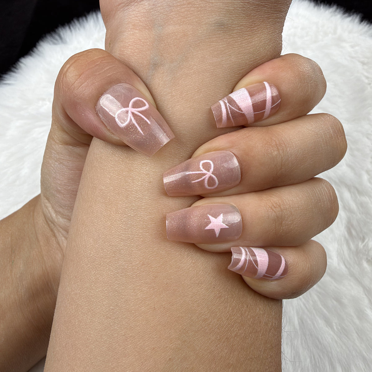Close-up of hands wearing Blush Ribbon nude pink coffin press-on nails with white ribbon and bow designs