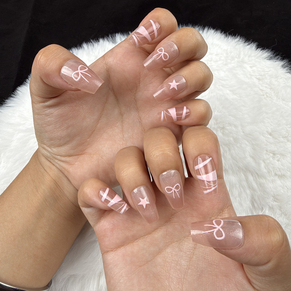 Hands wearing Blush Ribbon nude pink coffin press-on nails with white ribbon and bow designs