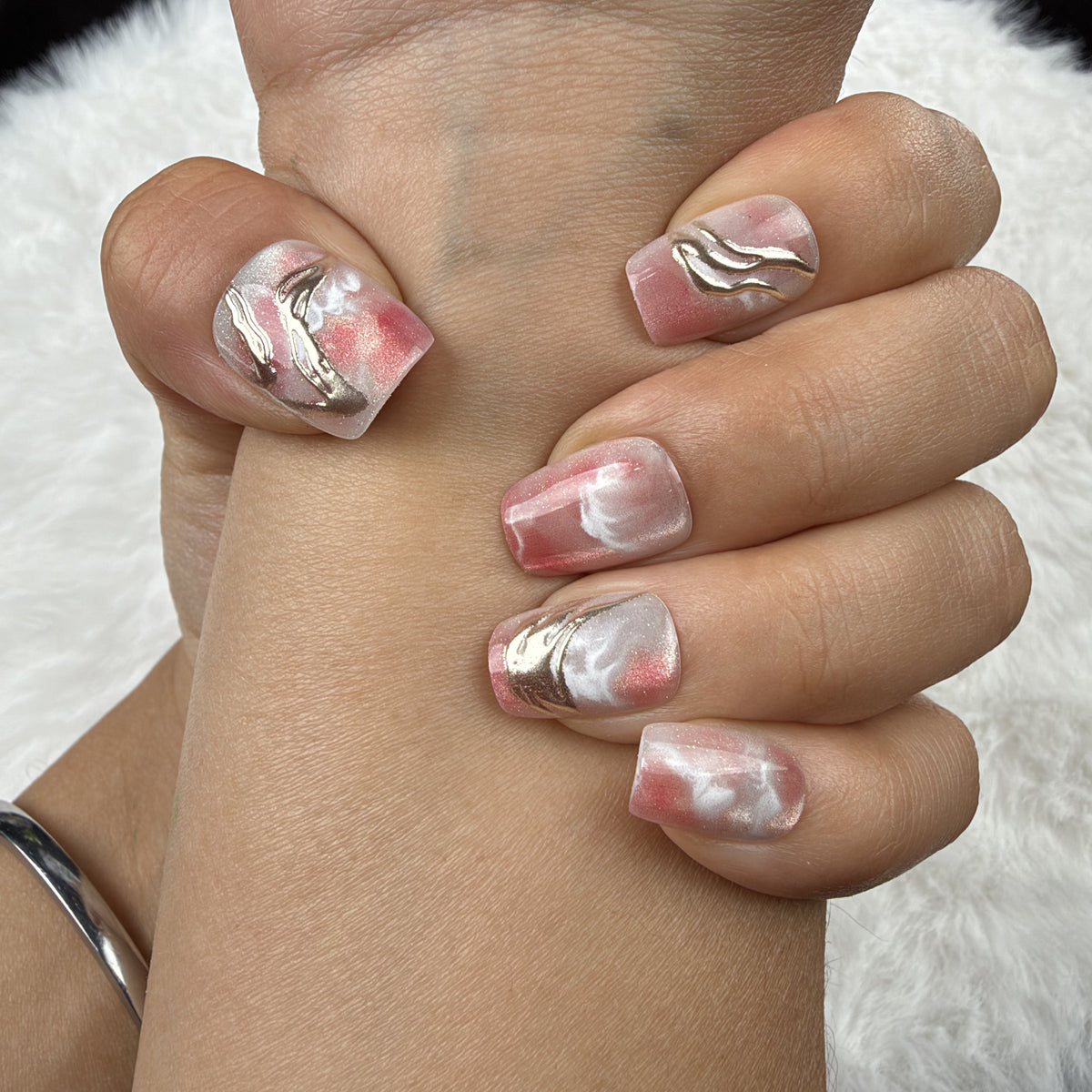 Close-up of hands wearing Rose Marble pink marble square press-on nails with metallic accents