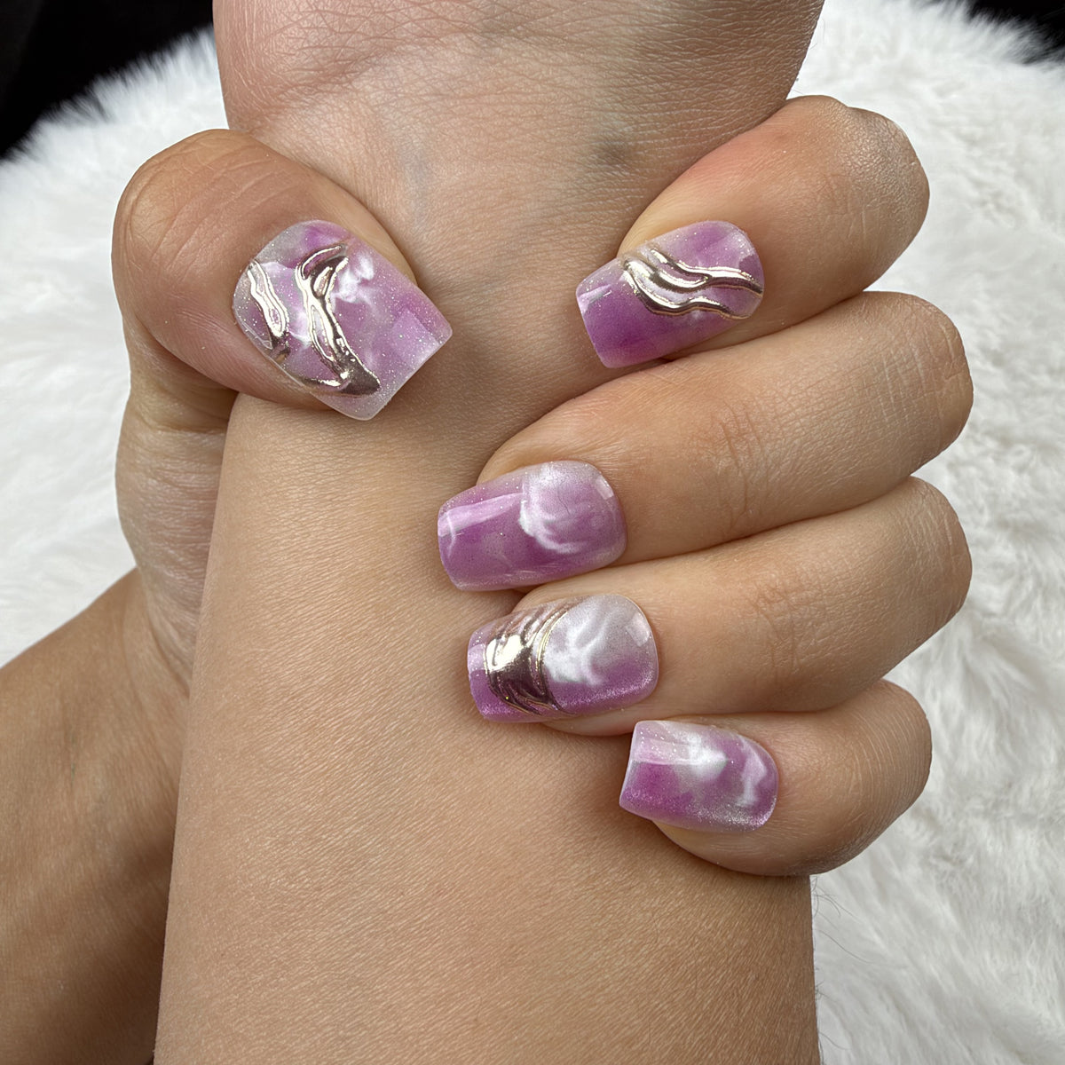 Close-up of hands wearing Orchid Marble purple marble square press-on nails with metallic accents