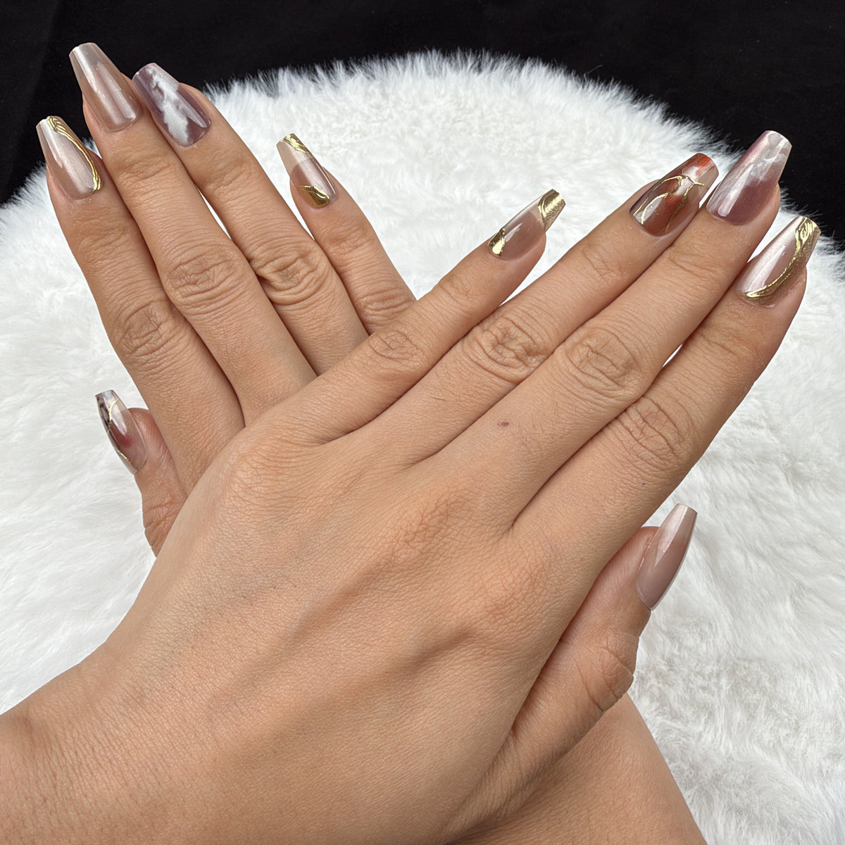 Detail shot of Amber Vein rose marble and gold-tone coffin press-on nails on hand