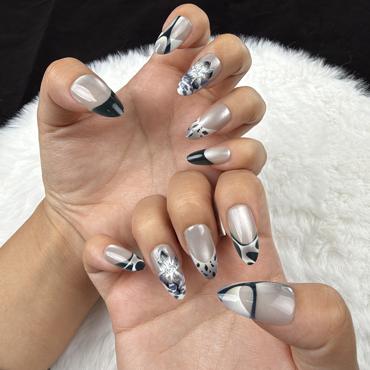 Hands wearing Midnight Iris black French tip and pearl white floral almond press-on nails