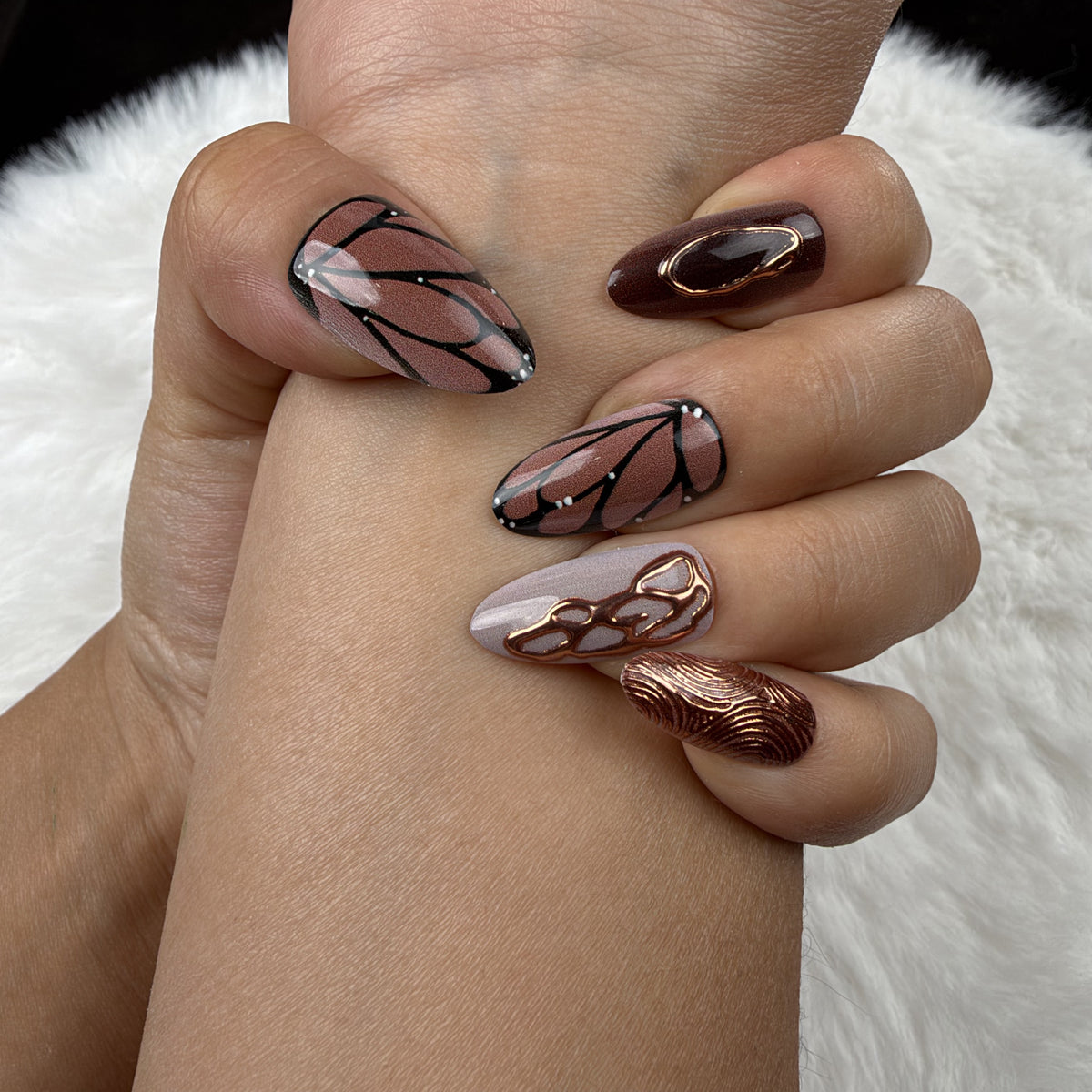 Close-up of hands wearing Copper Wings brown and copper butterfly wing almond press-on nails