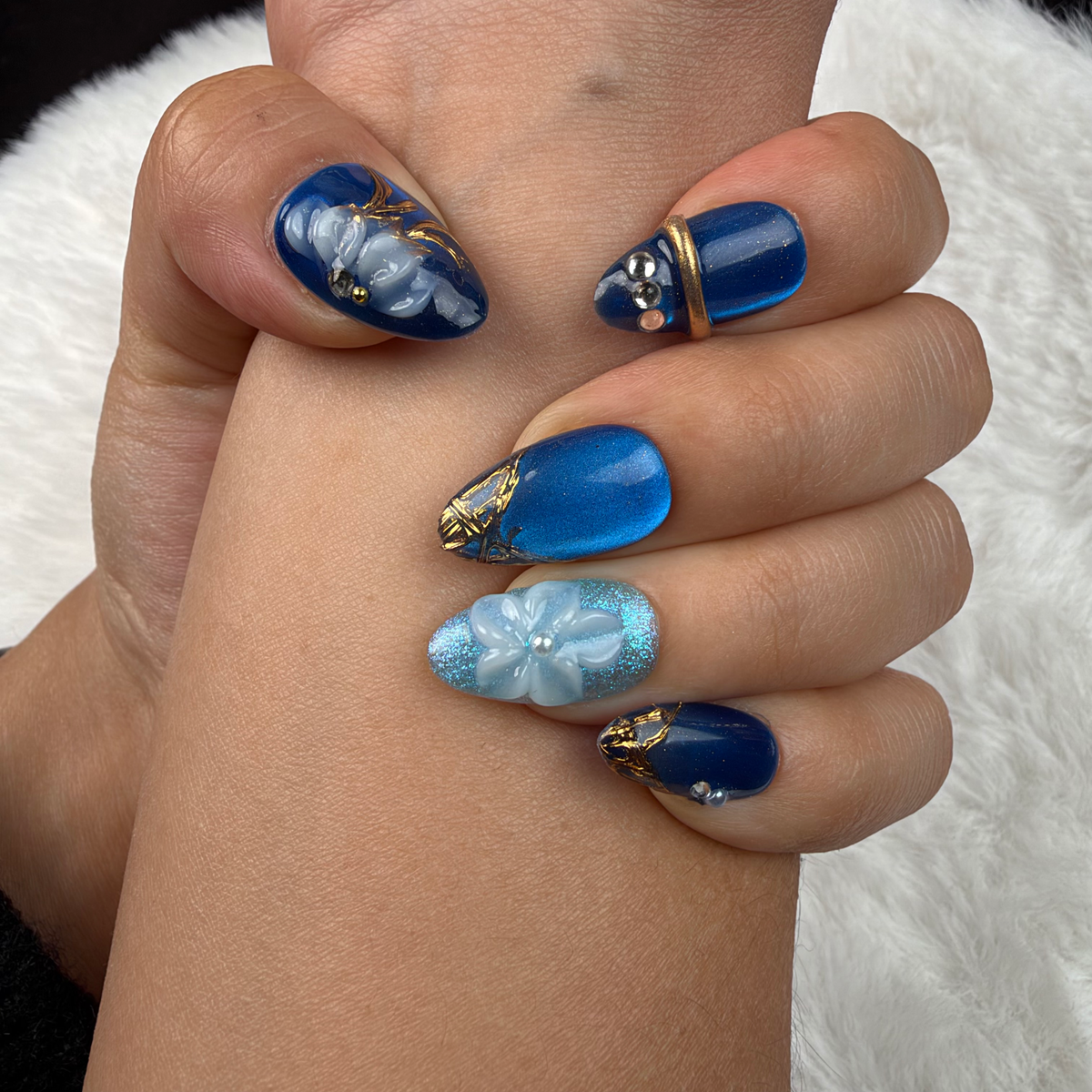 Detail shot of Blue Orchid cobalt and aqua floral almond press-on nails with gold lines on hand