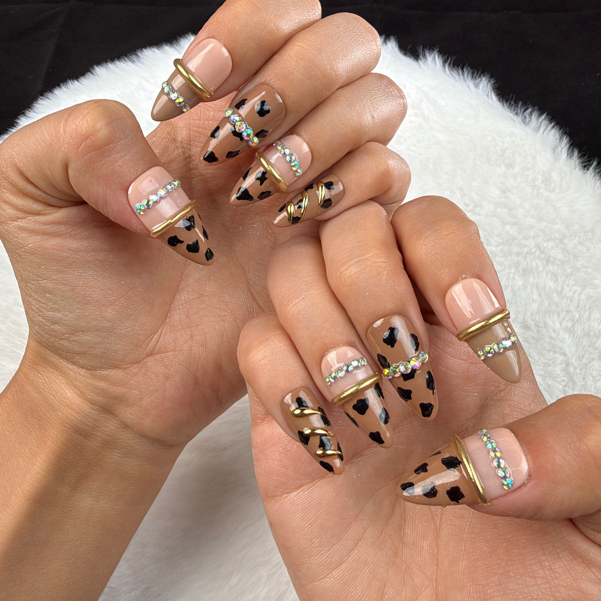 Hands wearing Wild Gleam nude leopard print almond press-on nails with gold accents and rhinestones