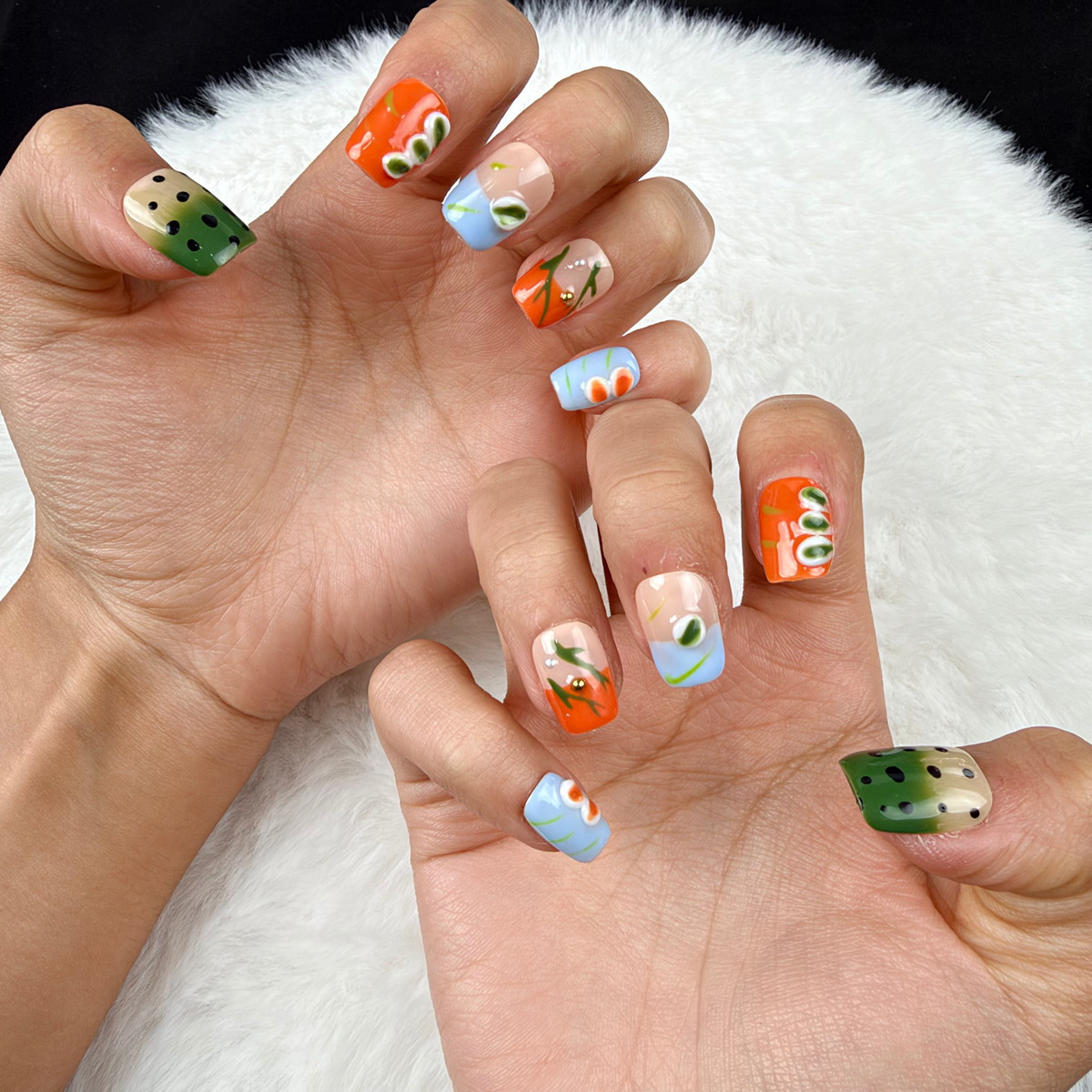 Close-up of hands wearing Summer Orchard orange, blue and green floral square press-on nails