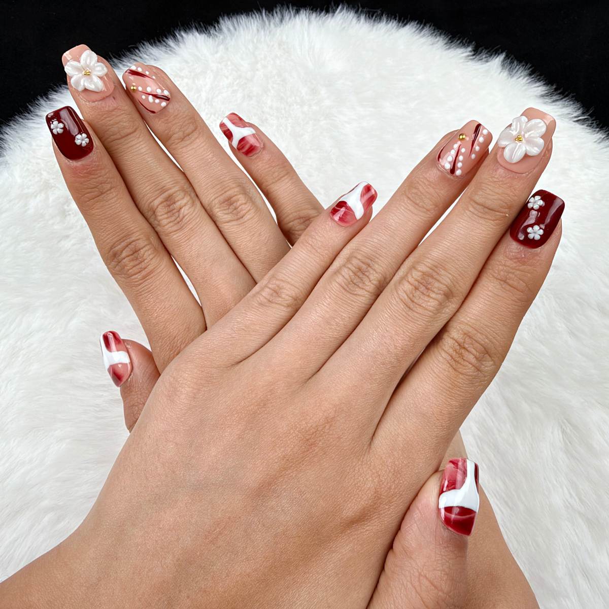 Hands wearing Burgundy Blossom burgundy and nude floral square press-on nails with white flowers