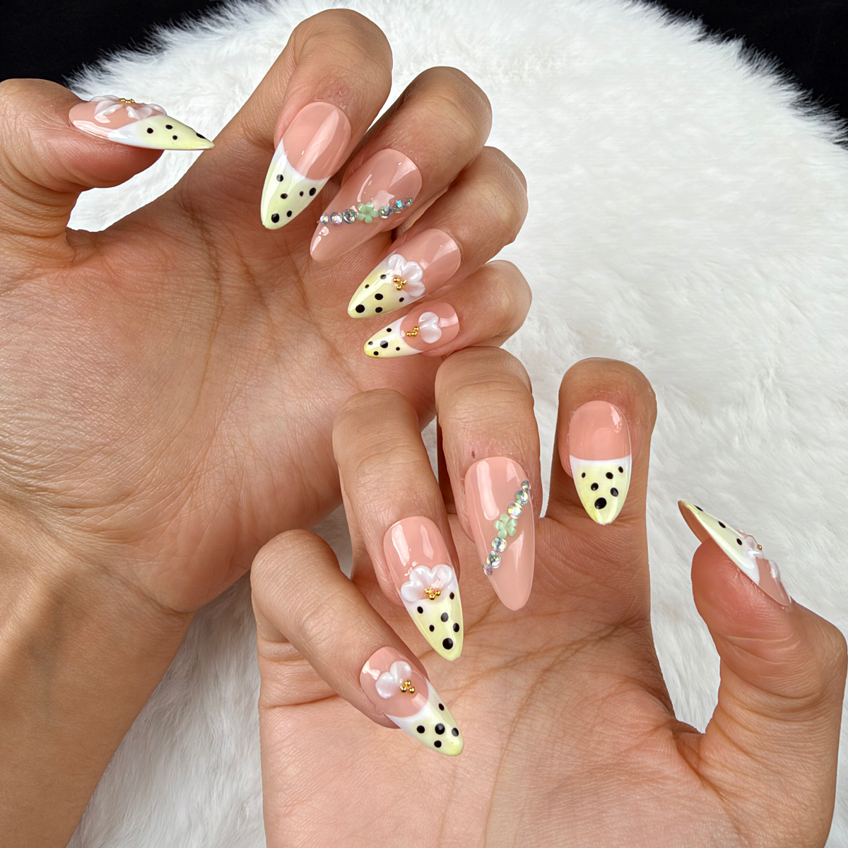 Close-up of hands wearing Lemon Blossom yellow polka dot French tip floral almond press-on nails